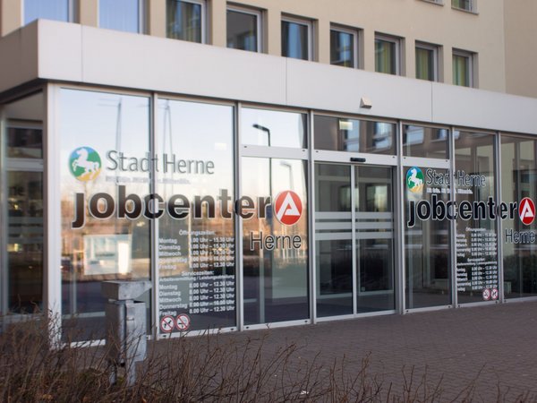 Eine Frontalaufnahme des Haupteinganges des jobcenter Herne in der Koniner Straße in Herne. Man sieht die gläsernen Windfang.